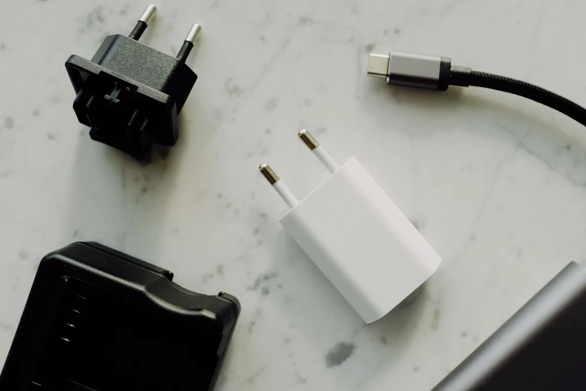 Adaptadores de tomada e um conector USB-C sobre uma superfície clara.