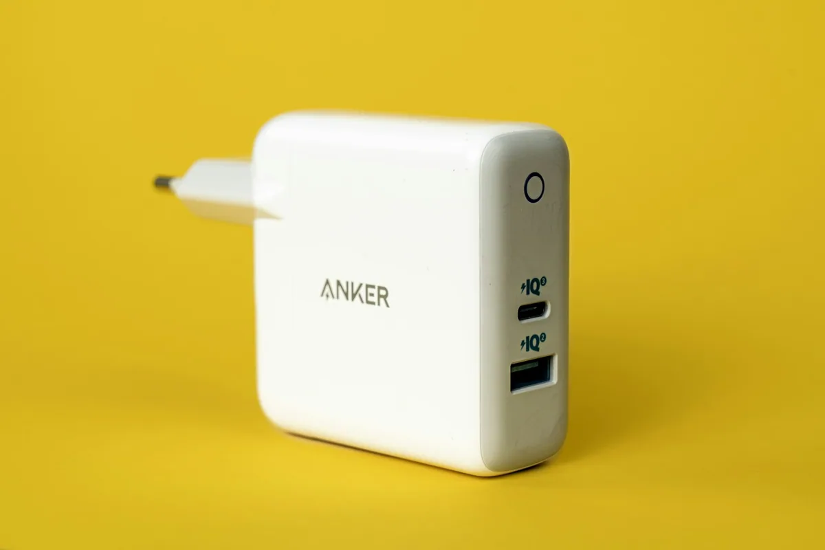 Carregador branco com portas USB-C e USB-A sobre fundo amarelo.