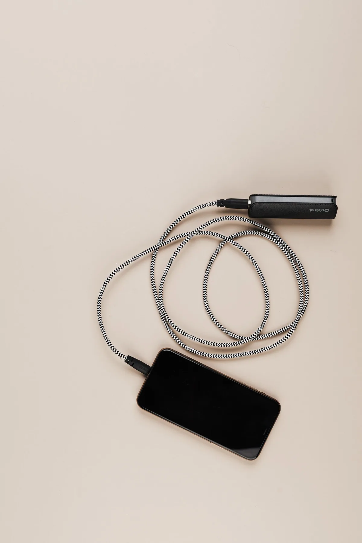 Celular conectado a uma bateria externa por um cabo sobre fundo bege.