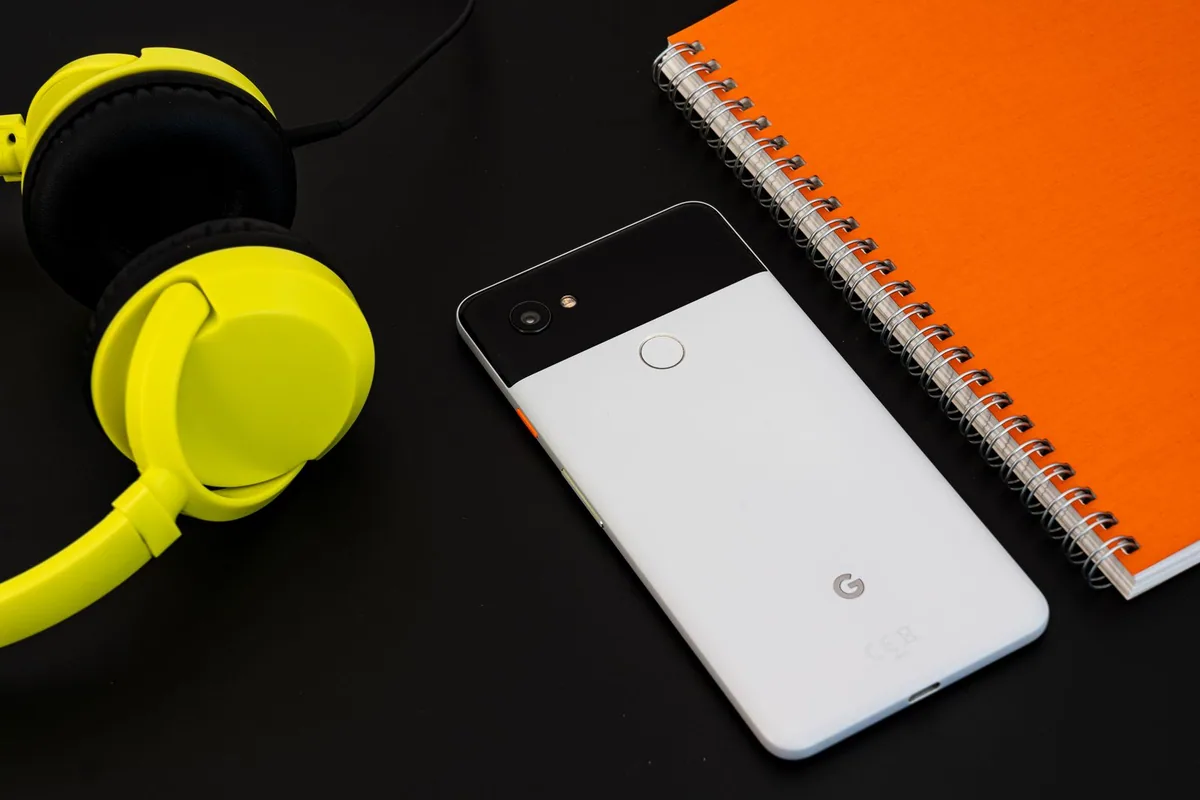 Celular, fones de ouvido e caderno sobre uma mesa.