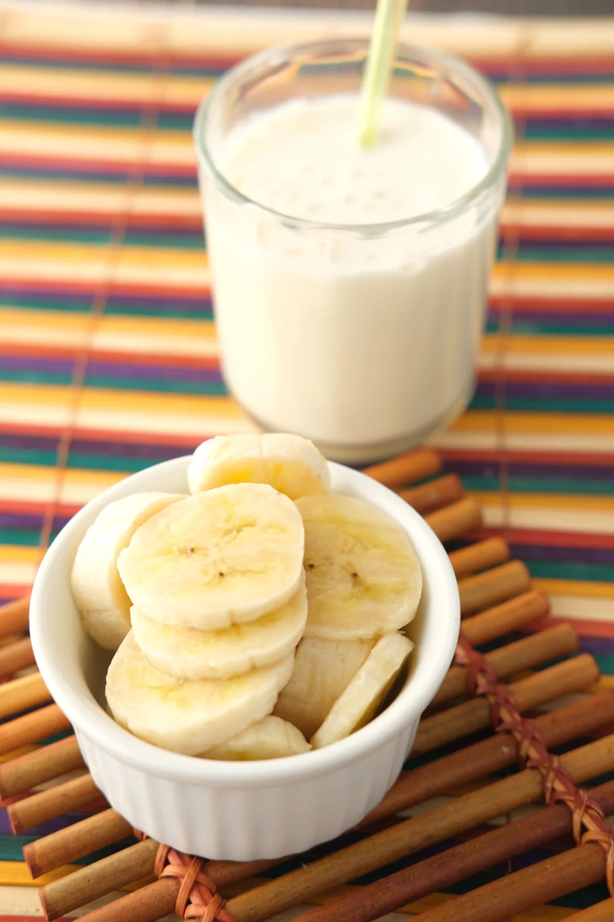 Banana em fatias numa tigela, com um copo de bebida cremosa ao fundo.