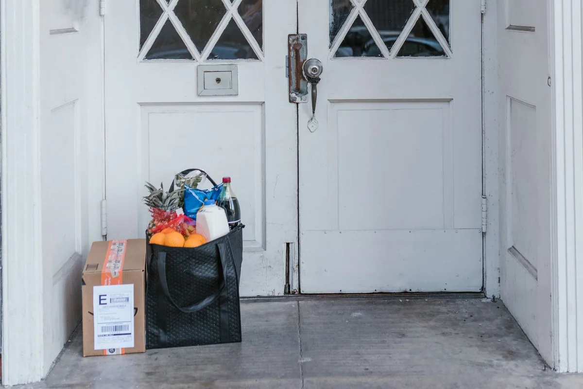 Caixa e sacola de compras entregues na entrada de uma casa.